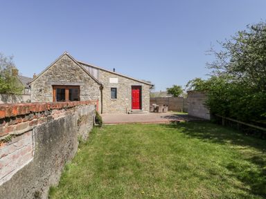A stone house with a red door a grass lawn and a patio with outdoor furniture at The Stone Barn in Evercreech near Shepton Mallet