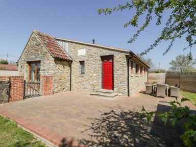 An outdoor patio with a stone building with a red door and outdoor table and chairs at The Stone Barn in Evercreech near Shepton Mallet