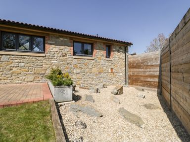 A stone wall building with a gravel area and large rocks beside a wooden fence at The Stone Barn in Evercreech near Shepton Mallet