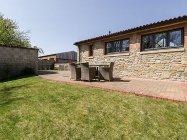 A patio with a dining table and six chairs next to a stone building with large windows at The Stone Barn in Evercreech near Shepton Mallet
