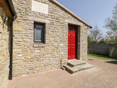Stone building with a red door and a small window next to it at The Stone Barn in Evercreech near Shepton Mallet