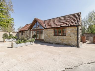 A stone house with tiled roof and large glass doors with wooden frames and planted flower containers outside at The Stone Barn in Evercreech near Shepton Mallet