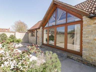 A stone building with large wooden framed glass doors and tiled roof with plants outside at The Stone Barn in Evercreech near Shepton Mallet