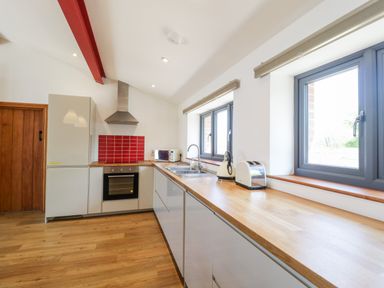 A kitchen with wooden floor and countertops stainless steel oven and hood white cabinets red tile backsplash and windows at The Stone Barn in Evercreech near Shepton Mallet