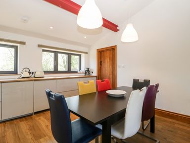 A dining room with a black table and multicolored chairs near kitchen cabinets and windows at The Stone Barn in Evercreech near Shepton Mallet