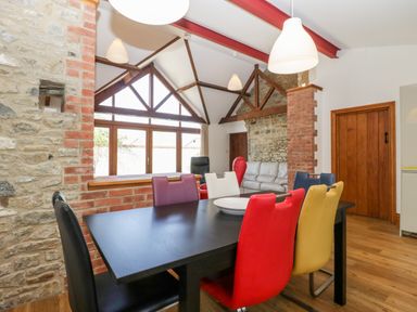 A dining area with a black table and multicolored chairs in a room with exposed stone and brick walls at The Stone Barn in Evercreech near Shepton Mallet