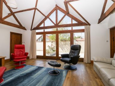 A sitting room with wooden beams red and black chairs a blue rug and large windows at The Stone Barn in Evercreech near Shepton Mallet