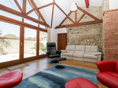 A living room with a beige sofa a black armchair a blue rug and large windows with wooden beams at The Stone Barn in Evercreech near Shepton Mallet
