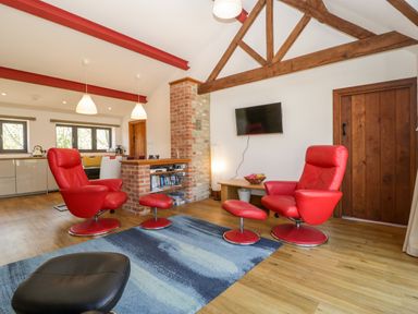 A living area with red chairs a blue rug a mounted television and exposed wooden beams at The Stone Barn in Evercreech near Shepton Mallet