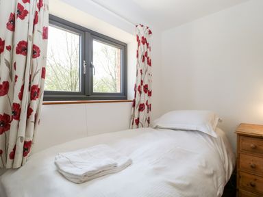 A small bedroom with a single bed white bedding floral curtains and a wooden bedside table at The Stone Barn in Evercreech near Shepton Mallet