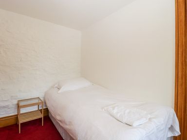 A small bedroom with a single bed white bedding a pillow and a folded towel on a red carpet at The Stone Barn in Evercreech near Shepton Mallet