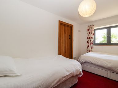 A bedroom with two single beds a wooden door a window with floral curtains and a round ceiling light at The Stone Barn in Evercreech near Shepton Mallet