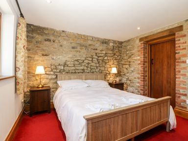 A bedroom with a wooden bed and bedside tables with lamps against a stone wall at The Stone Barn in Evercreech near Shepton Mallet