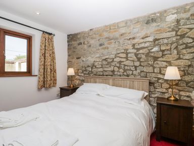 A bedroom with a bed between two bedside tables with lamps and a stone wall behind at The Stone Barn in Evercreech near Shepton Mallet
