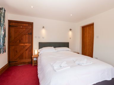 A bedroom with a double bed two wooden doors bedside tables and a red carpet at The Stone Barn in Evercreech near Shepton Mallet