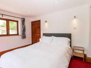 A bedroom with a double bed bedside table window and wooden door at The Stone Barn in Evercreech near Shepton Mallet