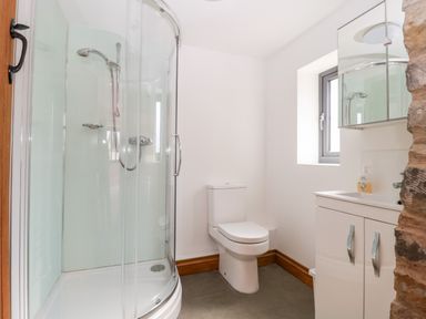 A bathroom with a curved glass shower, toilet, sink with cabinet, and a window at The Stone Barn in Evercreech near Shepton Mallet