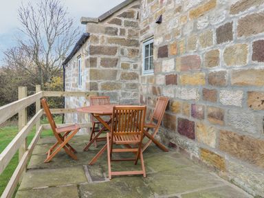A stone patio with wooden table and chairs next to a stone wall at Cottage Val in Ravenscar