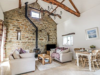 A living room with stone wall wood stove and dining table with chairs at Cottage Val in Ravenscar
