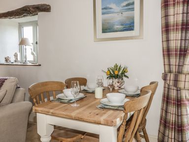 A dining table set with bowls wine glasses and a candle with wooden chairs near a window and a painting at Cottage Val in Ravenscar