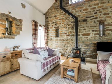 A living room with two sofas a wooden coffee table a wood-burning stove and stone walls at Cottage Val in Ravenscar