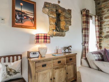 A corner with a wooden sideboard with a plaid lamp and horse figurines near a window with plaid curtains at Cottage Val in Ravenscar