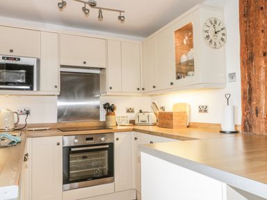 A kitchen with white cabinets wooden countertops a built in oven microwave kettle toaster and wall clock at Cottage Val in Ravenscar