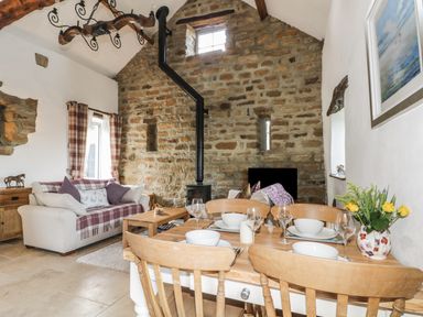 A living room with a dining table set with bowls glasses and flowers and a stone wall with a wood stove at Cottage Val in Ravenscar