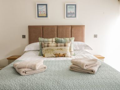 A bed with folded towels on a quilted bedspread and framed pictures on the wall at Cottage Val in Ravenscar