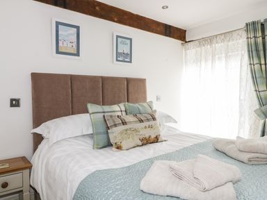 A bedroom with a bed with cushions and towels near a window with curtains at Cottage Val in Ravenscar
