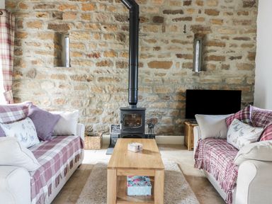 A living room with two sofas a wooden coffee table a wood burning stove and a television at Cottage Val in Ravenscar