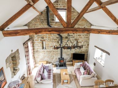 A living room with two sofas a wood stove a wooden coffee table and exposed wooden beams at Cottage Val in Ravenscar
