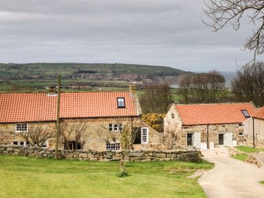 Stone houses with red tile roofs near a grassy area with a stone wall and hills in the background at Cottage Val in Ravenscar