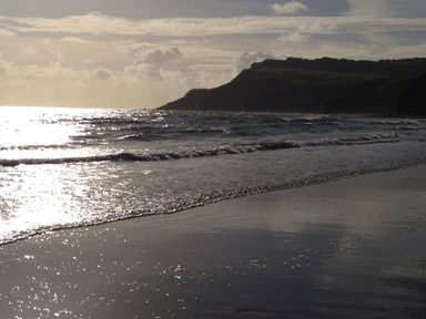 A beach with waves and a headland under a cloudy sky at Cottage Val in Ravenscar