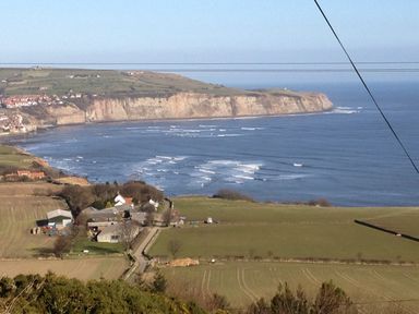 A coastal landscape with fields, farm buildings, a road, and cliffs by the sea at Cottage Val in Ravenscar