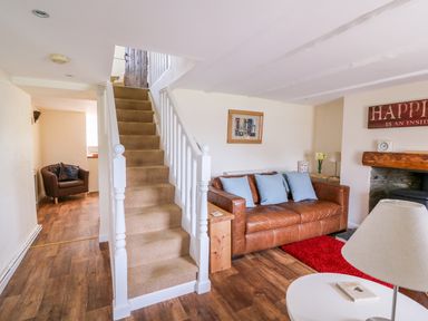 A living room with a brown leather sofa and blue cushions near a staircase at Bank House in Capel Iwan near Newcastle Emlyn