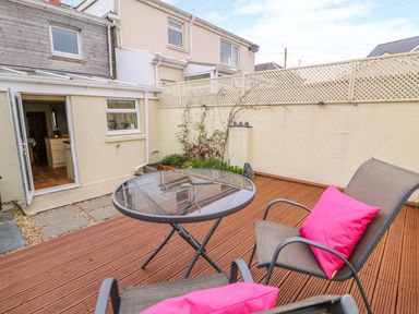 A small outdoor patio with a glass table and two chairs with pink cushions at Bank House in Capel Iwan near Newcastle Emlyn