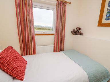 A bedroom with a single bed a red pillow striped curtains a window and a teddy bear at Bank House in Capel Iwan near Newcastle Emlyn