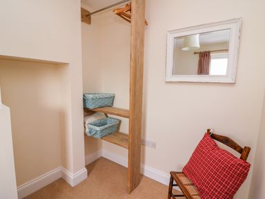 A small corner with wooden shelves and hanging rail with baskets a chair with a red cushion and a wall mirror at Bank House in Capel Iwan near Newcastle Emlyn