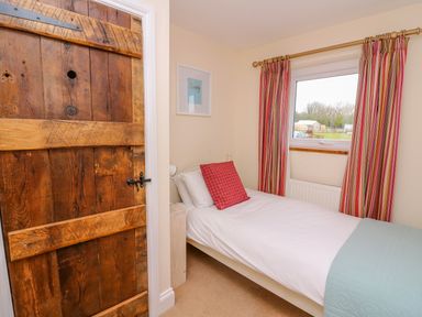 A bedroom with a single bed red plaid pillow striped curtains and a wooden door at Bank House in Capel Iwan near Newcastle Emlyn