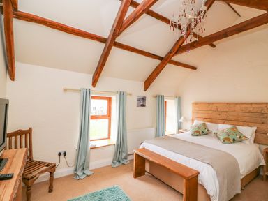 A bedroom with a bed bench wooden ceiling beams and two windows with curtains at Bank House in Capel Iwan near Newcastle Emlyn