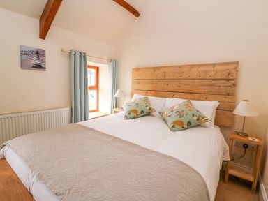 A bedroom with a wooden headboard bed two patterned cushions bedside tables with lamps and a window with light blue curtains at Bank House in Capel Iwan near Newcastle Emlyn