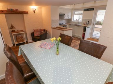A dining area with a polka dot tablecloth on the table and a kitchen with white cabinets in the background at Bank House in Capel Iwan near Newcastle Emlyn