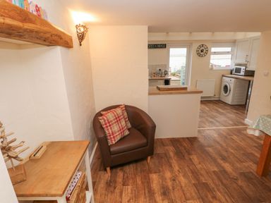 A room with a brown armchair with two cushions a wooden table a partial view of a kitchen with a washing machine a microwave and a clock on the wall at Bank House in Capel Iwan near Newcastle Emlyn