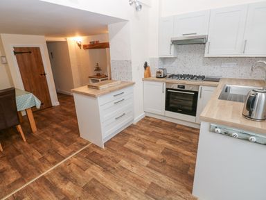 A kitchen with wooden floors white cabinets a gas stove oven and a kettle at Bank House in Capel Iwan near Newcastle Emlyn