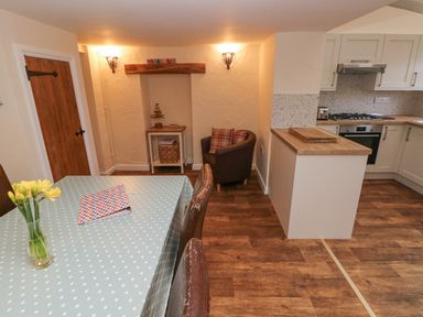 A kitchen and dining area with a wooden table covered with a polka dot tablecloth and yellow flowers in a vase at Bank House in Capel Iwan near Newcastle Emlyn