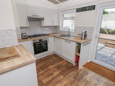 A kitchen with white cabinets wooden countertops a gas stove oven toaster kettle a window and a door to patio at Bank House in Capel Iwan near Newcastle Emlyn