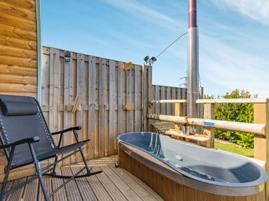 An outdoor wooden deck with a black reclining chair and a hot tub with a metal chimney at Two Hoots in Northop