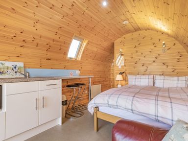 A bedroom with a bed kitchen counter stools and wooden paneled walls at Two Hoots in Northop
