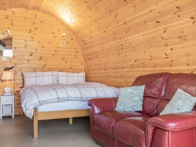 A bedroom with a bed a nightstand and a red leather sofa with cushions at Two Hoots in Northop